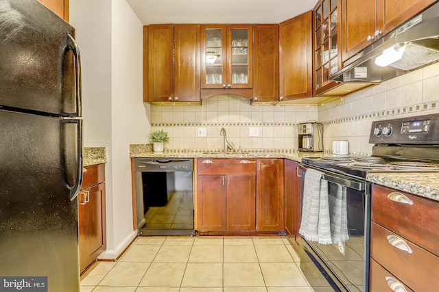 kitchen with light tile patterned flooring, decorative backsplash, light stone countertops, and black appliances