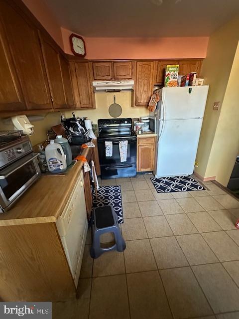 kitchen featuring white fridge, light tile patterned floors, and black / electric stove