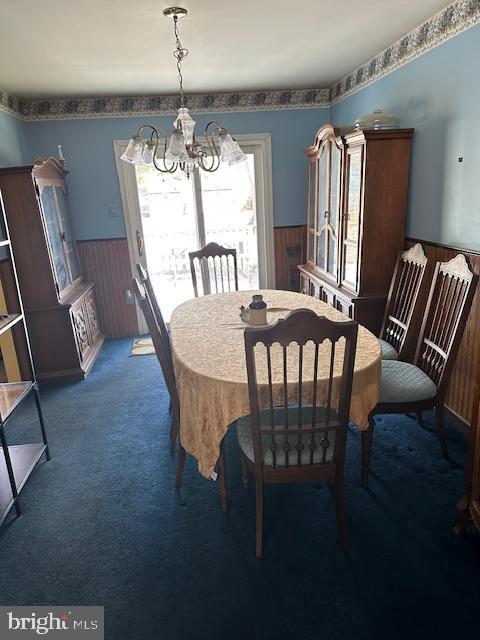 dining area featuring wood walls, carpet floors, and a chandelier