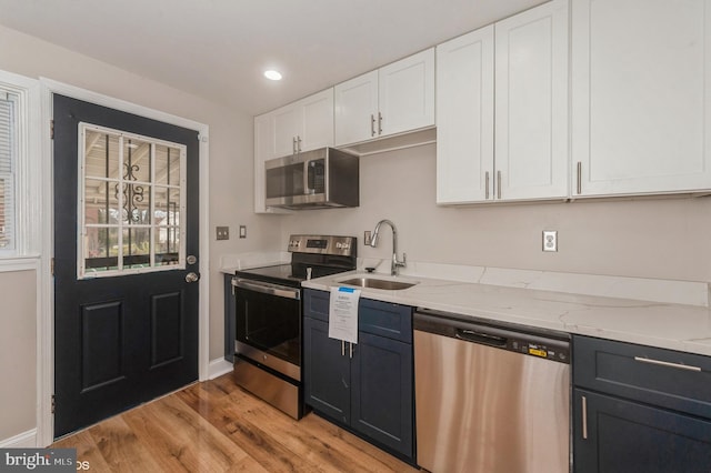 kitchen featuring white cabinets, sink, light stone countertops, light wood-type flooring, and stainless steel appliances