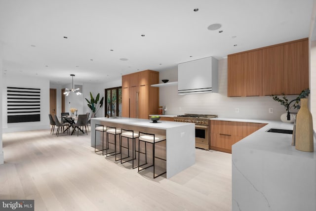 kitchen with hanging light fixtures, light hardwood / wood-style flooring, high end stove, a kitchen bar, and a kitchen island