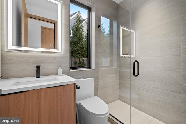 bathroom featuring vanity, toilet, a shower with door, and tile walls