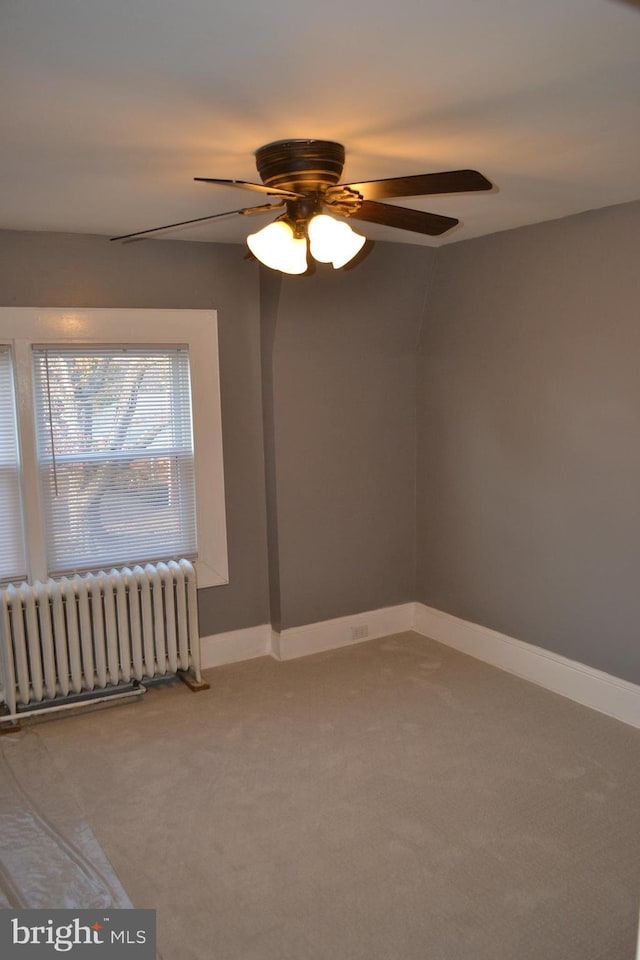 unfurnished room featuring carpet, radiator, and ceiling fan