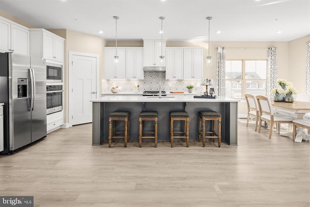 kitchen with decorative light fixtures, stainless steel appliances, white cabinetry, and a kitchen island with sink