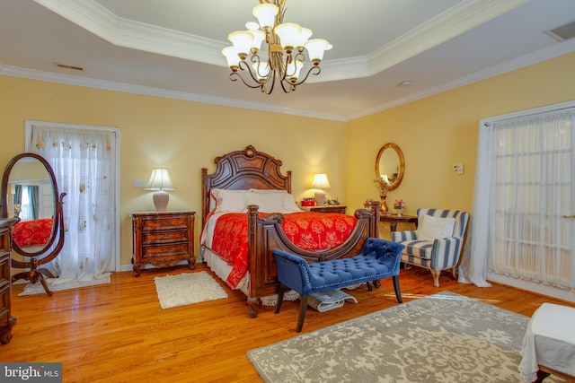 bedroom featuring hardwood / wood-style flooring, ornamental molding, a tray ceiling, and an inviting chandelier