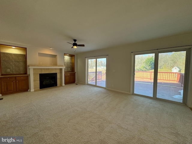 unfurnished living room with a tile fireplace, ceiling fan, and light colored carpet