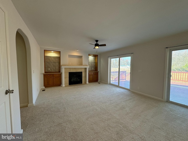 unfurnished living room featuring ceiling fan, light colored carpet, and a tiled fireplace