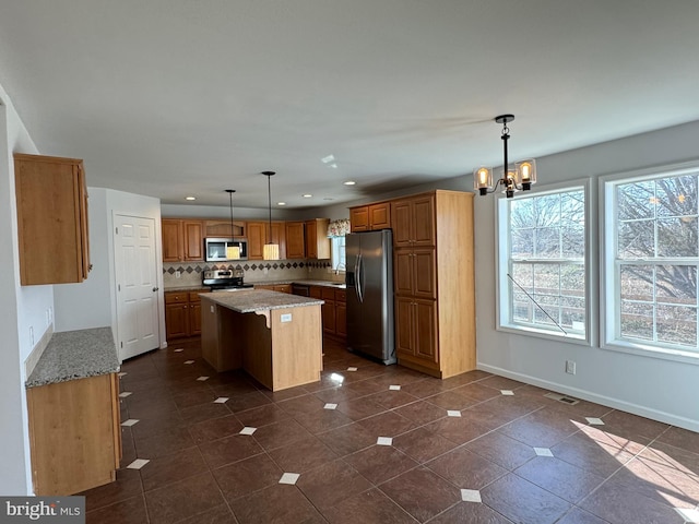 kitchen featuring decorative backsplash, light stone countertops, stainless steel appliances, a center island, and hanging light fixtures