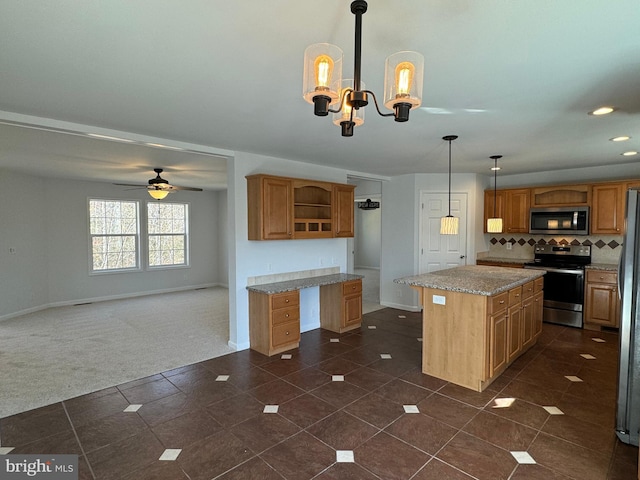 kitchen featuring pendant lighting, ceiling fan with notable chandelier, light stone countertops, a kitchen island, and stainless steel appliances