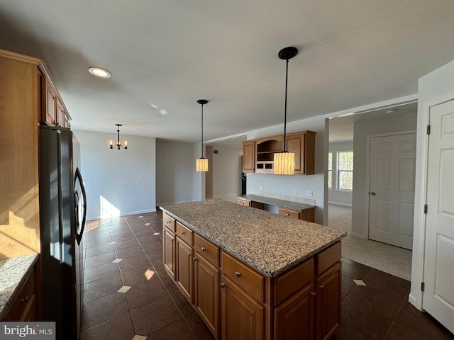 kitchen featuring black refrigerator, pendant lighting, a kitchen island, and light stone countertops