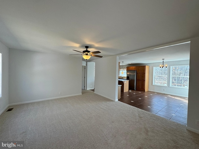 unfurnished living room with dark tile patterned flooring and ceiling fan with notable chandelier