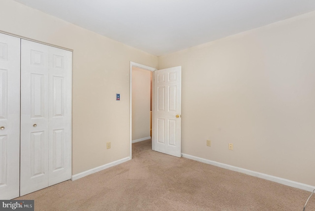 unfurnished bedroom featuring a closet, light colored carpet, and baseboards