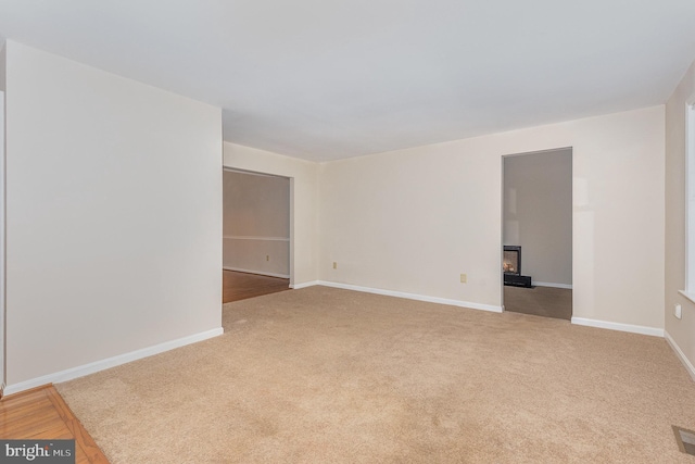 empty room with carpet, a glass covered fireplace, and baseboards