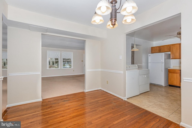 unfurnished dining area featuring light wood-style floors, baseboards, ceiling fan with notable chandelier, and washing machine and clothes dryer