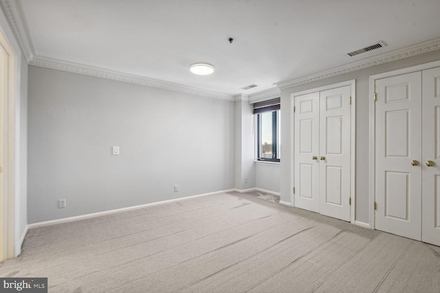 unfurnished bedroom featuring ornamental molding, light carpet, and two closets