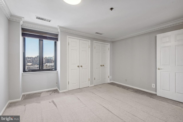 unfurnished bedroom with ornamental molding, light carpet, and multiple closets