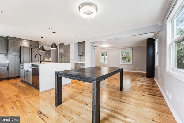 kitchen featuring dishwasher, decorative light fixtures, a center island with sink, and light hardwood / wood-style flooring