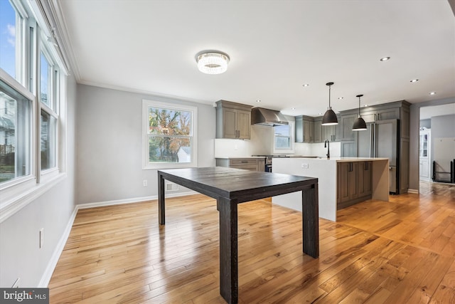 kitchen featuring a wealth of natural light, a center island with sink, wall chimney exhaust hood, and hanging light fixtures