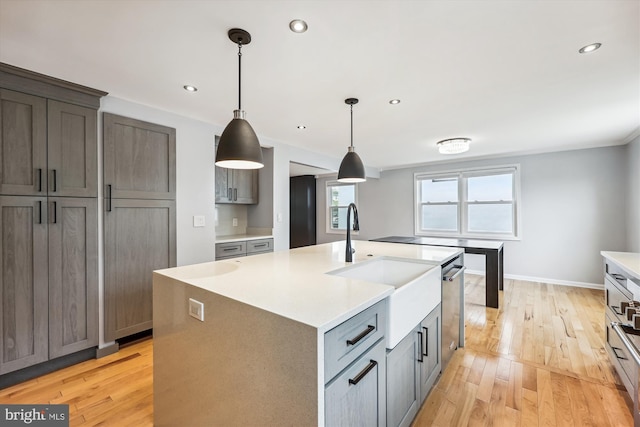 kitchen featuring decorative light fixtures, a center island with sink, light hardwood / wood-style flooring, and sink