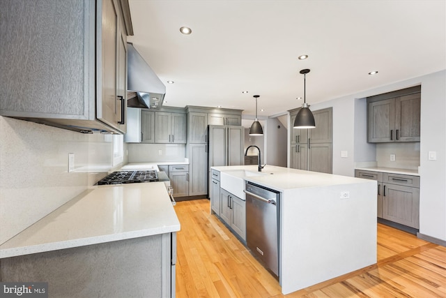 kitchen featuring exhaust hood, sink, decorative light fixtures, dishwasher, and an island with sink