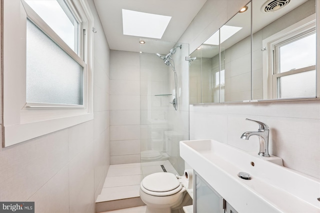 bathroom featuring vanity, toilet, tiled shower, and a skylight