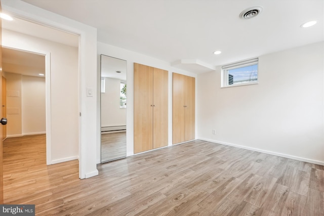 unfurnished bedroom featuring multiple closets, light hardwood / wood-style flooring, and a baseboard radiator