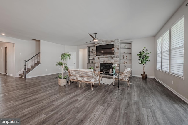 living room featuring dark hardwood / wood-style flooring, a stone fireplace, and ceiling fan