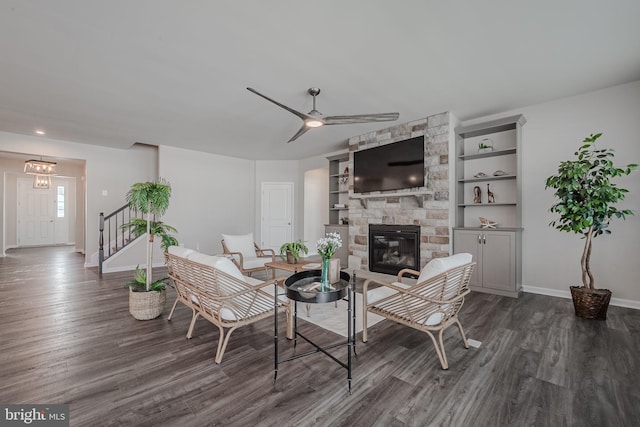 living room with ceiling fan, a stone fireplace, dark hardwood / wood-style flooring, and built in shelves