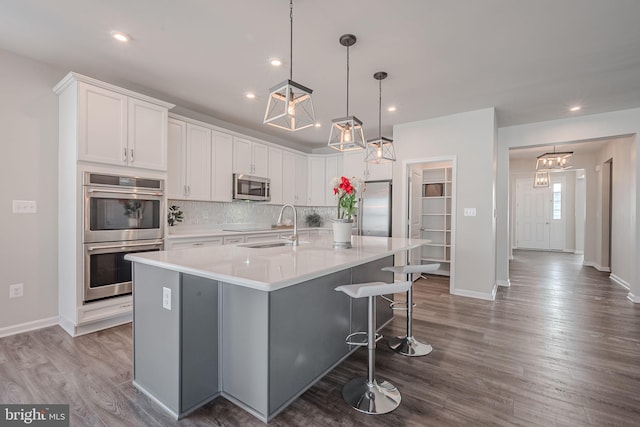 kitchen with dark hardwood / wood-style flooring, stainless steel appliances, white cabinetry, and a center island with sink