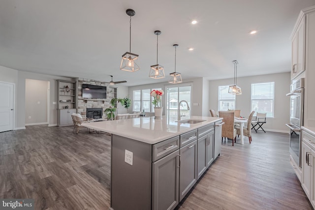 kitchen with an island with sink, a stone fireplace, a wealth of natural light, and sink