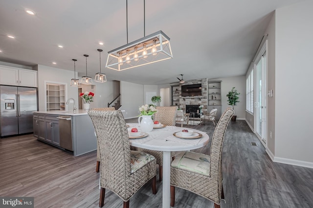 dining space featuring dark hardwood / wood-style flooring, ceiling fan, a stone fireplace, and sink