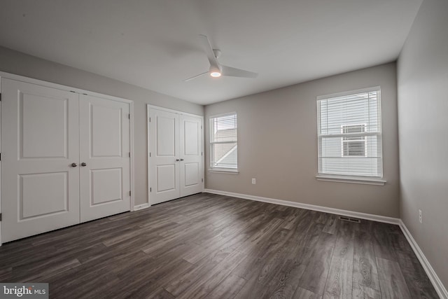 unfurnished bedroom with multiple windows, ceiling fan, and dark wood-type flooring