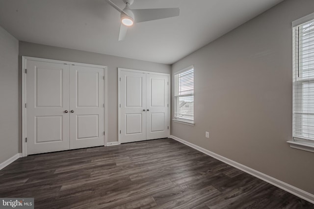 unfurnished bedroom with dark hardwood / wood-style floors, ceiling fan, multiple closets, and multiple windows