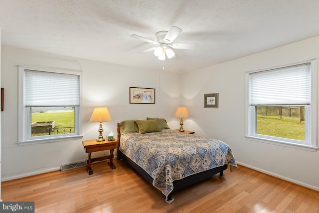 bedroom with multiple windows, ceiling fan, and wood-type flooring