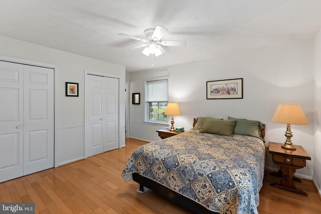 bedroom featuring a textured ceiling, ceiling fan, wood-type flooring, and two closets