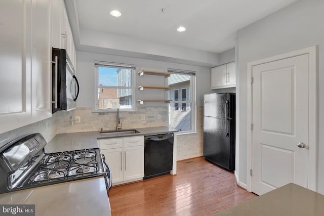 kitchen featuring light wood-type flooring, tasteful backsplash, sink, black appliances, and white cabinets