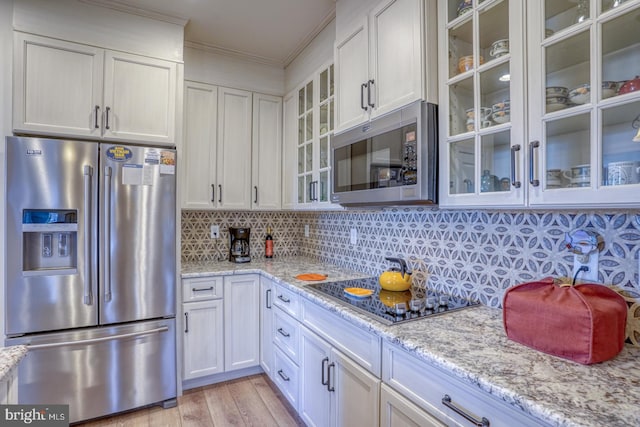 kitchen with light stone countertops, tasteful backsplash, ornamental molding, stainless steel appliances, and white cabinetry