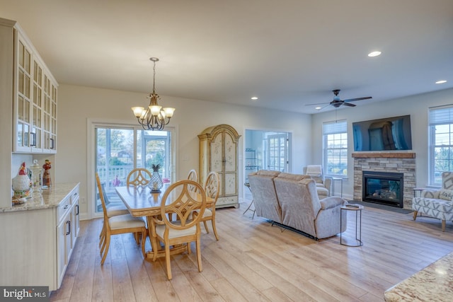 dining space featuring ceiling fan with notable chandelier, light hardwood / wood-style floors, and a stone fireplace