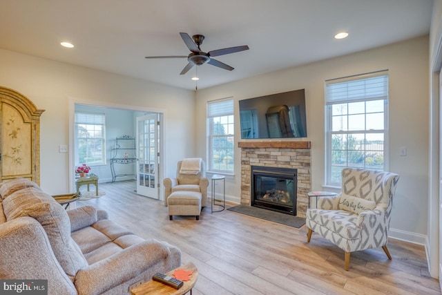 living room featuring ceiling fan, a stone fireplace, and light hardwood / wood-style flooring