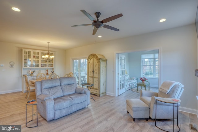 living room with ceiling fan with notable chandelier and light wood-type flooring