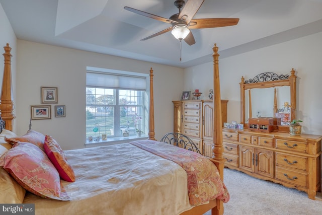 bedroom with light colored carpet, a raised ceiling, and ceiling fan