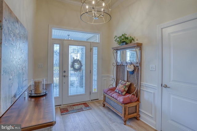 entrance foyer with an inviting chandelier, ornamental molding, and light hardwood / wood-style flooring