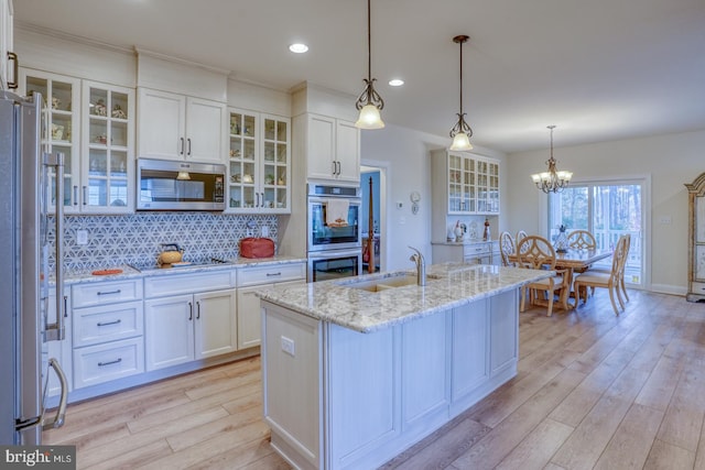 kitchen with white cabinets, sink, light hardwood / wood-style flooring, an island with sink, and appliances with stainless steel finishes