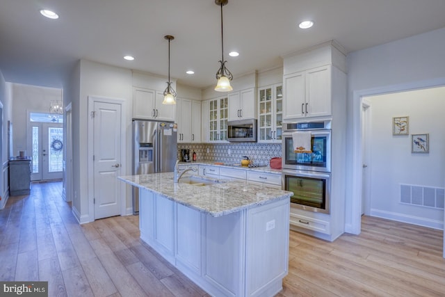 kitchen with appliances with stainless steel finishes, a kitchen island with sink, sink, light hardwood / wood-style flooring, and white cabinetry