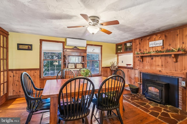 dining area with hardwood / wood-style floors, a wall mounted air conditioner, a wood stove, wooden walls, and ceiling fan