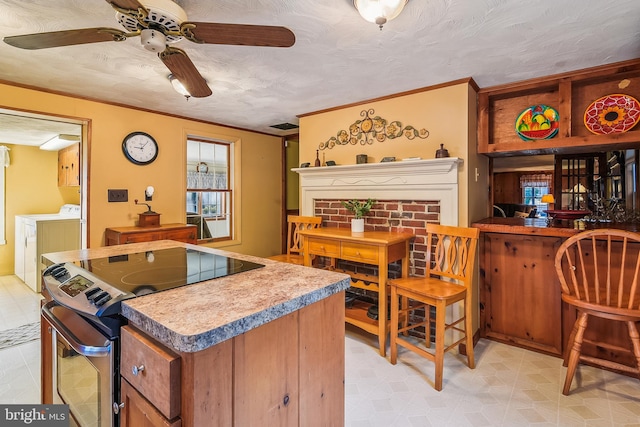 kitchen featuring washing machine and clothes dryer, ceiling fan, stainless steel range with electric cooktop, and a textured ceiling