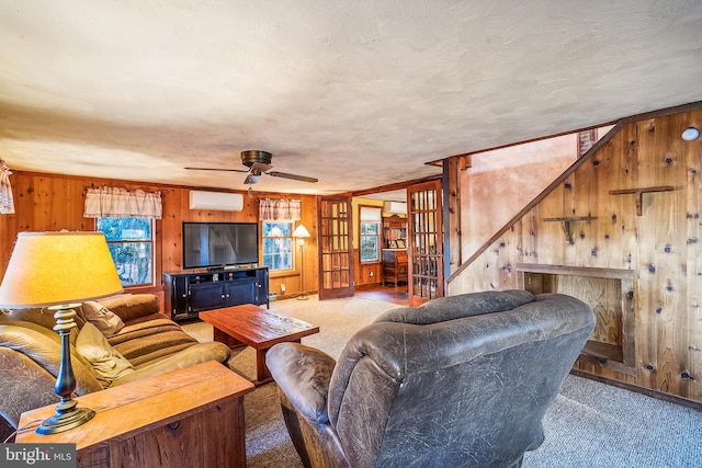 carpeted living room with a wall mounted air conditioner, french doors, ceiling fan, and wooden walls