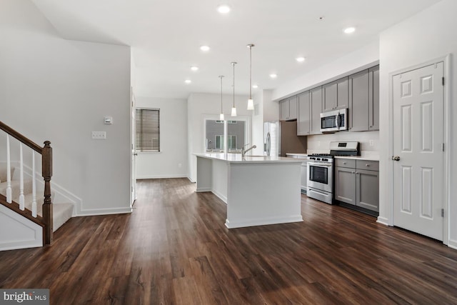 kitchen featuring gray cabinetry, hanging light fixtures, stainless steel appliances, dark hardwood / wood-style flooring, and an island with sink