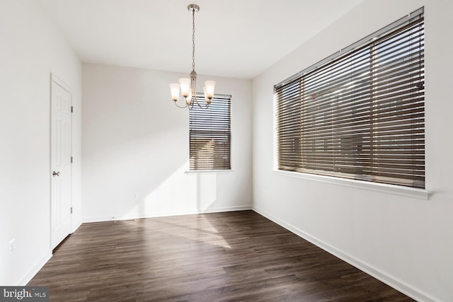 unfurnished dining area featuring a wealth of natural light, dark wood-type flooring, and an inviting chandelier