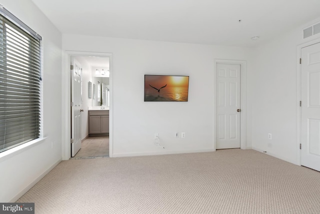 unfurnished bedroom featuring connected bathroom and light carpet